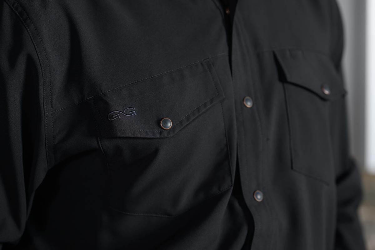 Close-up of a black button-front shirt with chest pockets and metallic snap buttons, worn by a person.