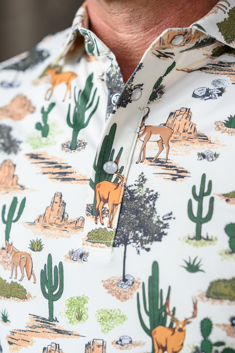 Close-up of a button-down shirt featuring a desert landscape print with cacti, rock formations, and deer on an off-white background.