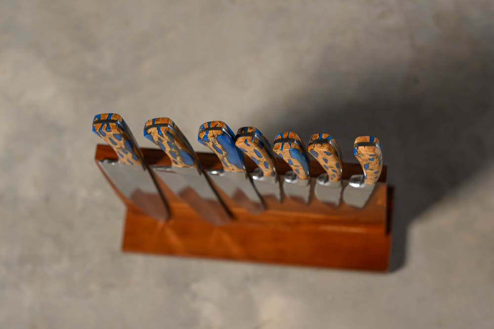 A set of knives with patterned blue and orange handles, displayed in a wooden knife block on a gray concrete surface.