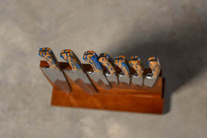 A set of knives with patterned blue and orange handles, displayed in a wooden knife block on a gray concrete surface.
