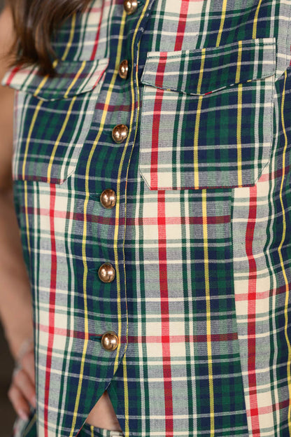 Close-up of a plaid button-front garment with green, red, yellow, and white stripes, featuring metallic gold buttons and flap chest pockets.