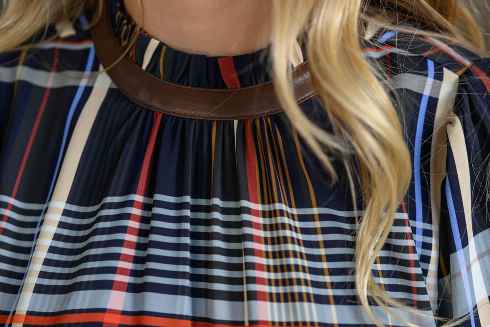 Close-up of a person wearing a navy plaid top with red, beige, and light blue stripes, featuring a brown faux-leather collar.