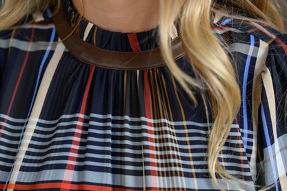 Close-up of a person wearing a navy plaid top with red, beige, and light blue stripes, featuring a brown faux-leather collar.