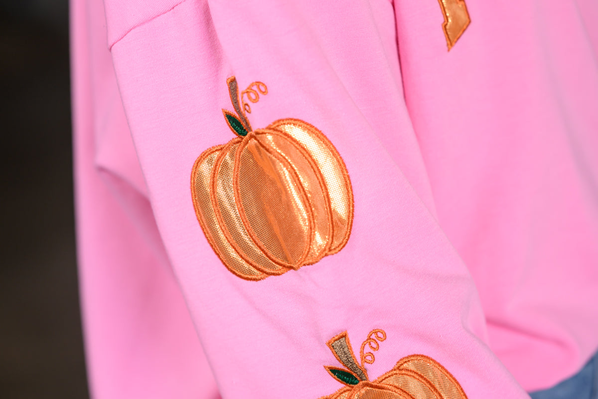 Close-up of a pink garment featuring embroidered metallic orange pumpkins with small green leaves and brown stems.