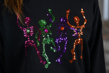 Close-up of a black sweatshirt featuring four sequined dancing skeleton figures in pink, green, purple, and orange, with a person's hair visible at the top left.