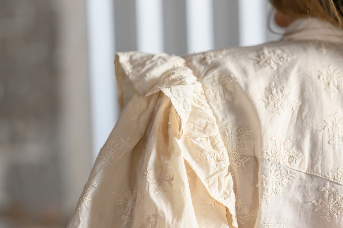 Close-up of tonal floral embroidery and ruffled shoulder detail on Sister Mary Annie ivory top