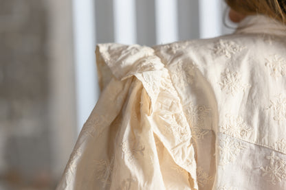 Close-up of tonal floral embroidery and ruffled shoulder detail on Sister Mary Annie ivory top