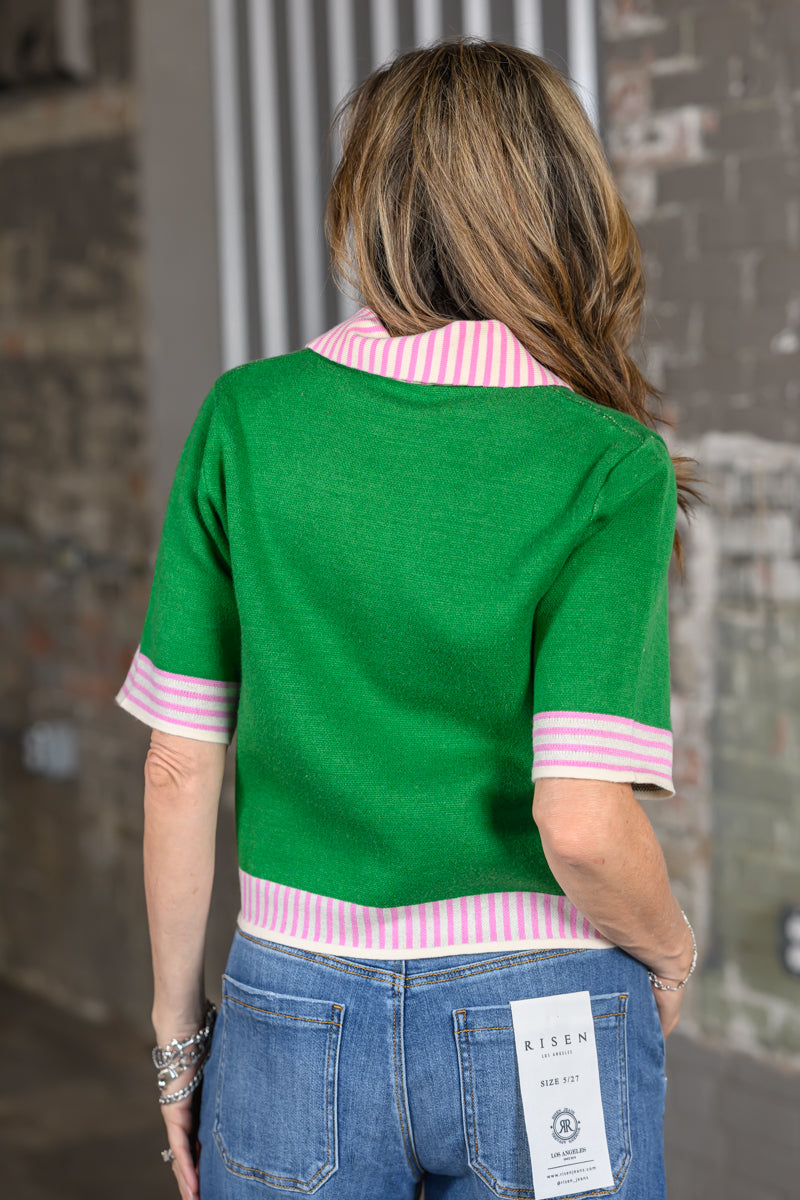 Back view of green waist-length cardigan with short sleeves and pink-and-cream striped collar, cuffs and hem
