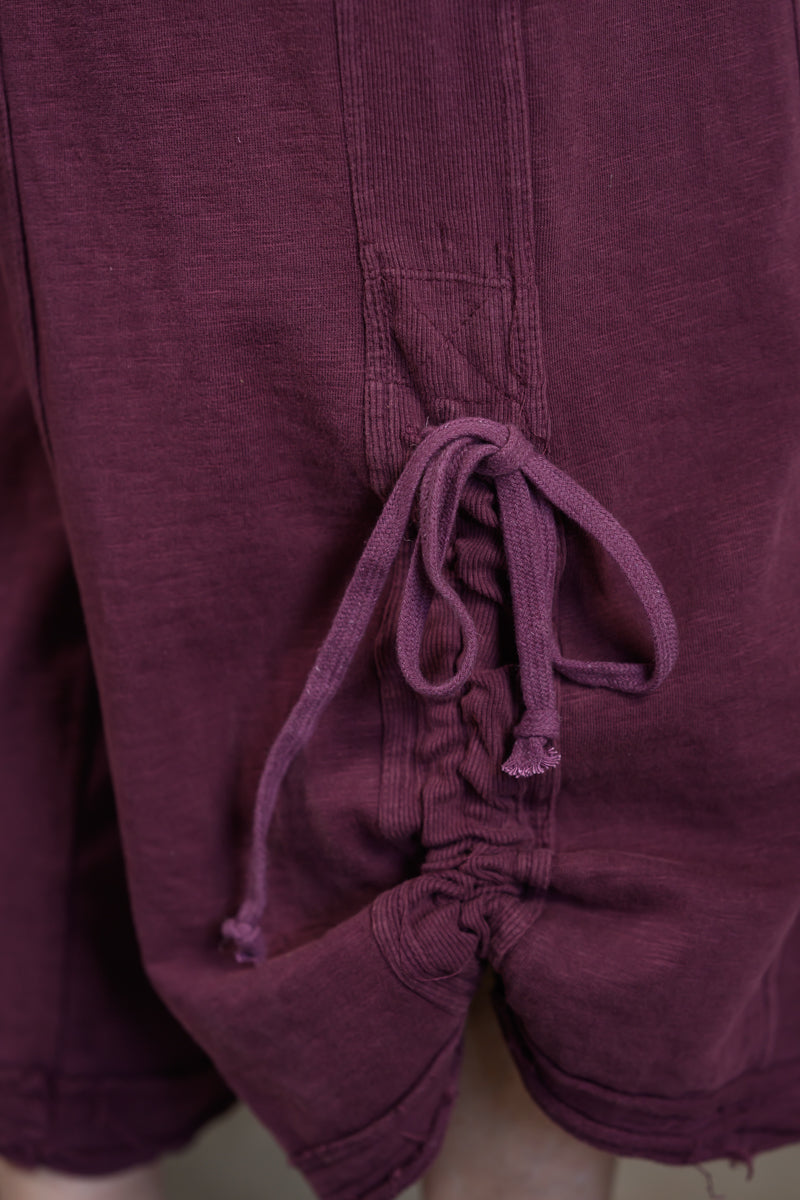 Close-up of a of dark plum purple jumpsuit showing the drawstring waist and textured fabric.