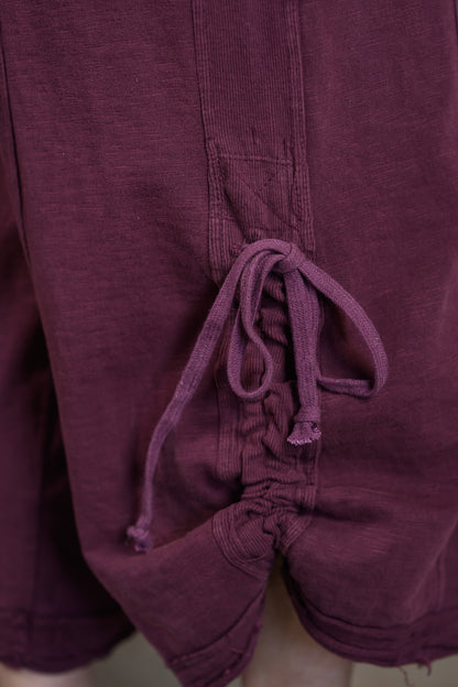 Close-up of a of dark plum purple jumpsuit showing the drawstring waist and textured fabric.