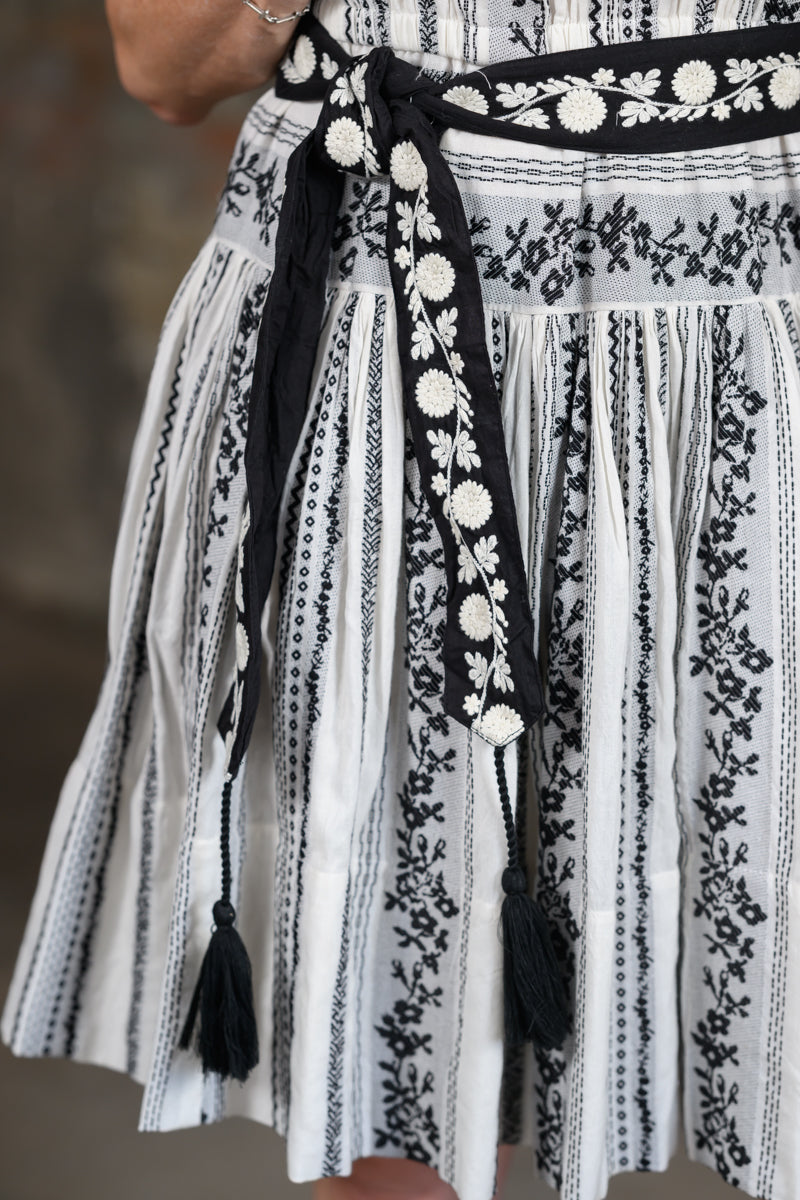 Close-up of a black and white patterned skirt with vertical stripes, floral embroidery, and a matching tie belt with tassels.