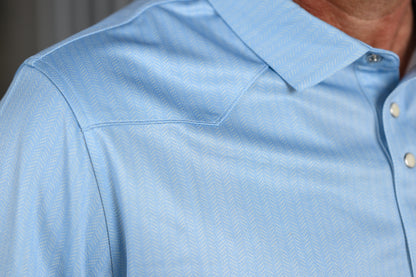 Close-up of a light blue textured button-down shirt on a model, showing the collar, shoulder seam, and white buttons.