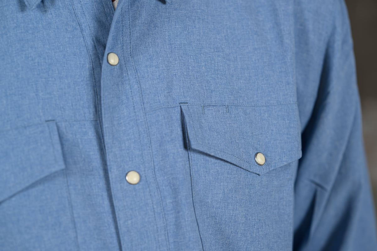 Close-up of a blue textured button-up shirt with white buttons and a chest pocket, worn by a person.