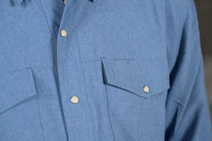 Close-up of a blue textured button-up shirt with white buttons and a chest pocket, worn by a person.