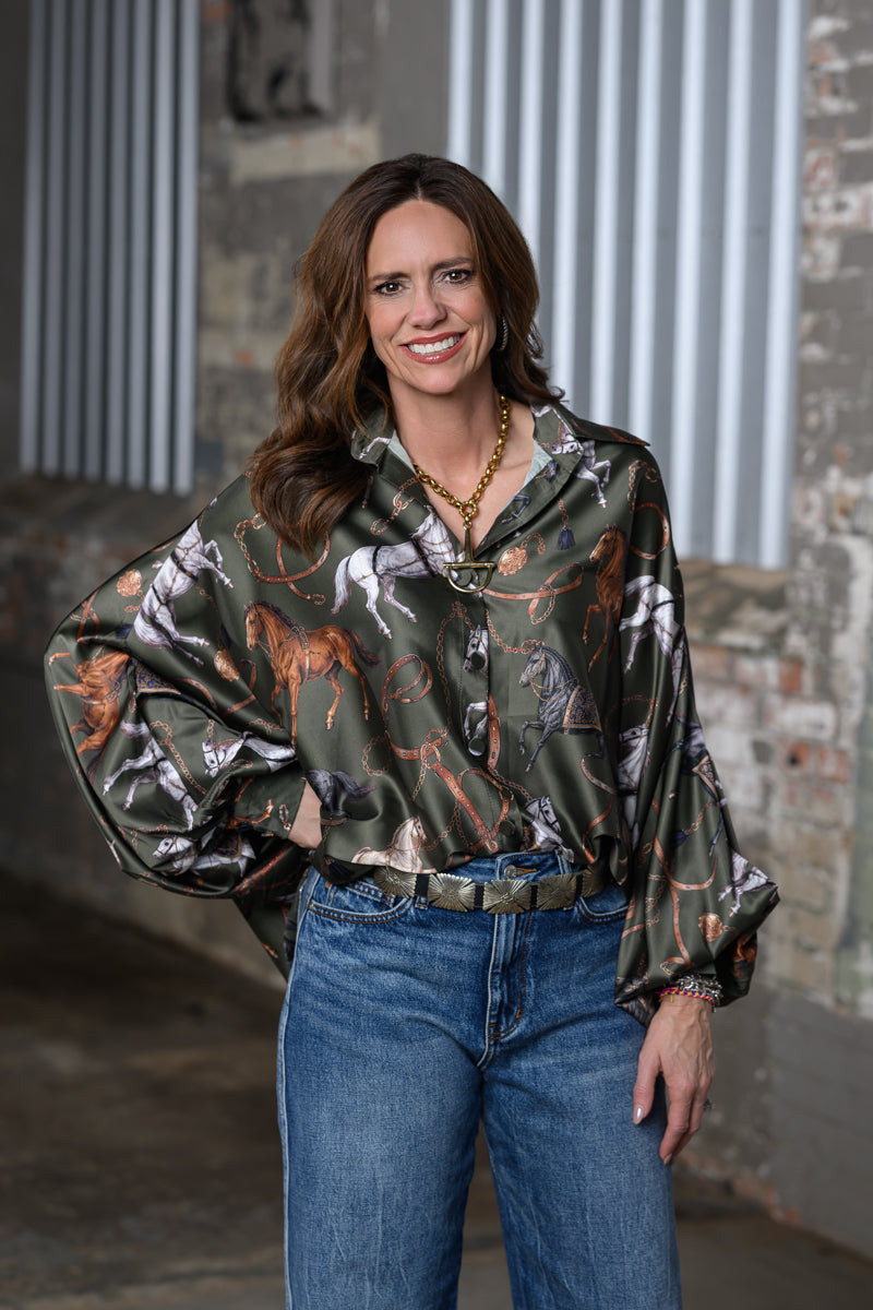 Jennifer Smith STS Ranch 1930 Remnant modeling the Beulah Style horse print top in olive green, front 3/4 view with one hand on hip.