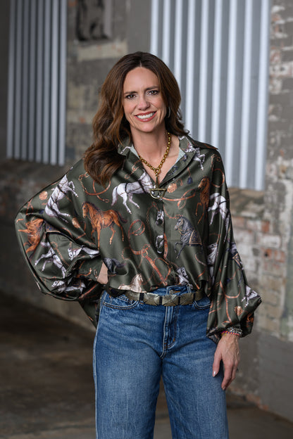 Jennifer Smith STS Ranch 1930 Remnant modeling the Beulah Style horse print top in olive green, front 3/4 view with one hand on hip.