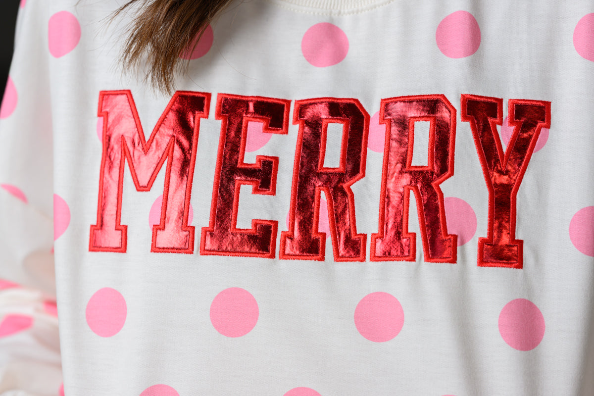 A close-up of a white sweatshirt with pink polka dots and large metallic red 'MERRY' lettering across the chest.