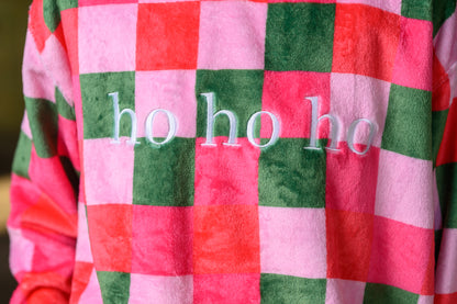 A close-up of a plush fleece sweatshirt with a pink and green checkered pattern and the words 'ho ho ho' embroidered in white across the center.