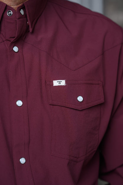 Close-up of a burgundy western-style button-down shirt with a chest pocket and a small white label featuring a monogram logo.