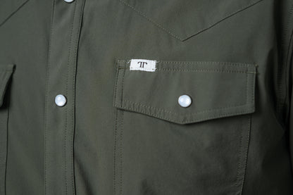 Close-up of an olive green western-style shirt jacket featuring a chest pocket with a white snap button and a small white brand label with a black monogram.