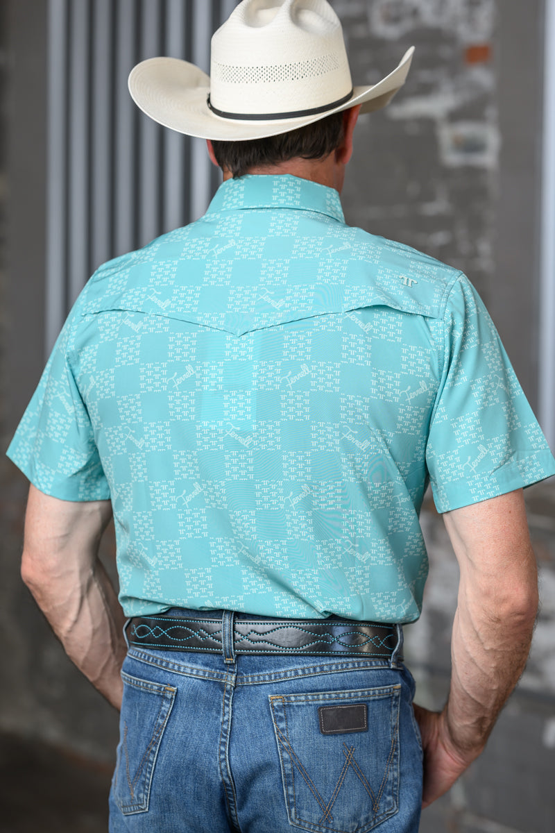 A man viewed from behind wearing a light turquoise short-sleeve western shirt with a subtle geometric pattern, blue jeans, and a white cowboy hat.