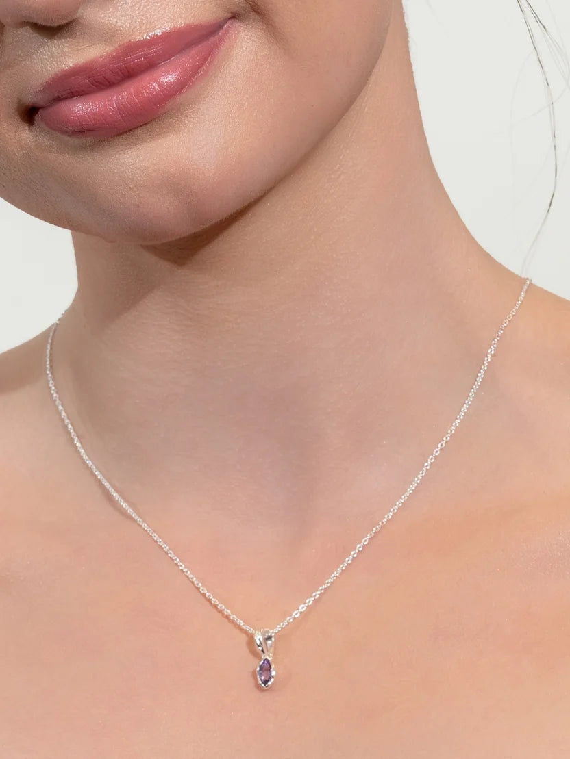 A close-up of a model's neck and lower face wearing a delicate silver chain necklace with a small teardrop-shaped purple gemstone pendant.