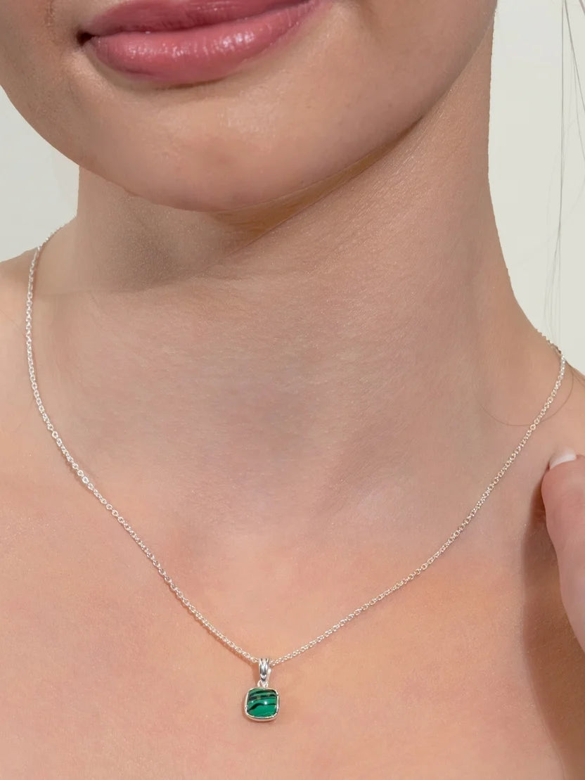 A close-up of a model wearing a delicate silver chain necklace with a small square-cut green pendant.