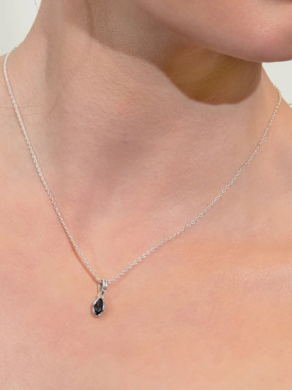 A close-up of a delicate silver chain necklace with a small teardrop-shaped dark gemstone pendant, worn on a model's neck.
