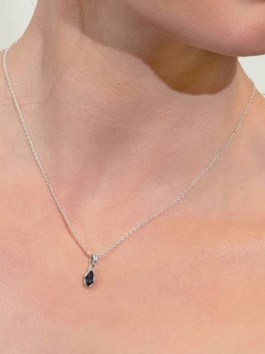 A close-up of a delicate silver chain necklace with a small teardrop-shaped dark gemstone pendant, worn on a model's neck.
