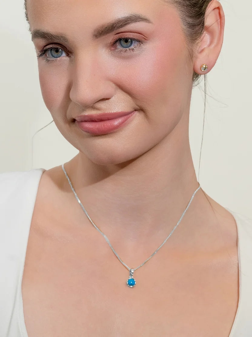 Woman wearing a silver necklace with a blue pendant on a plain background