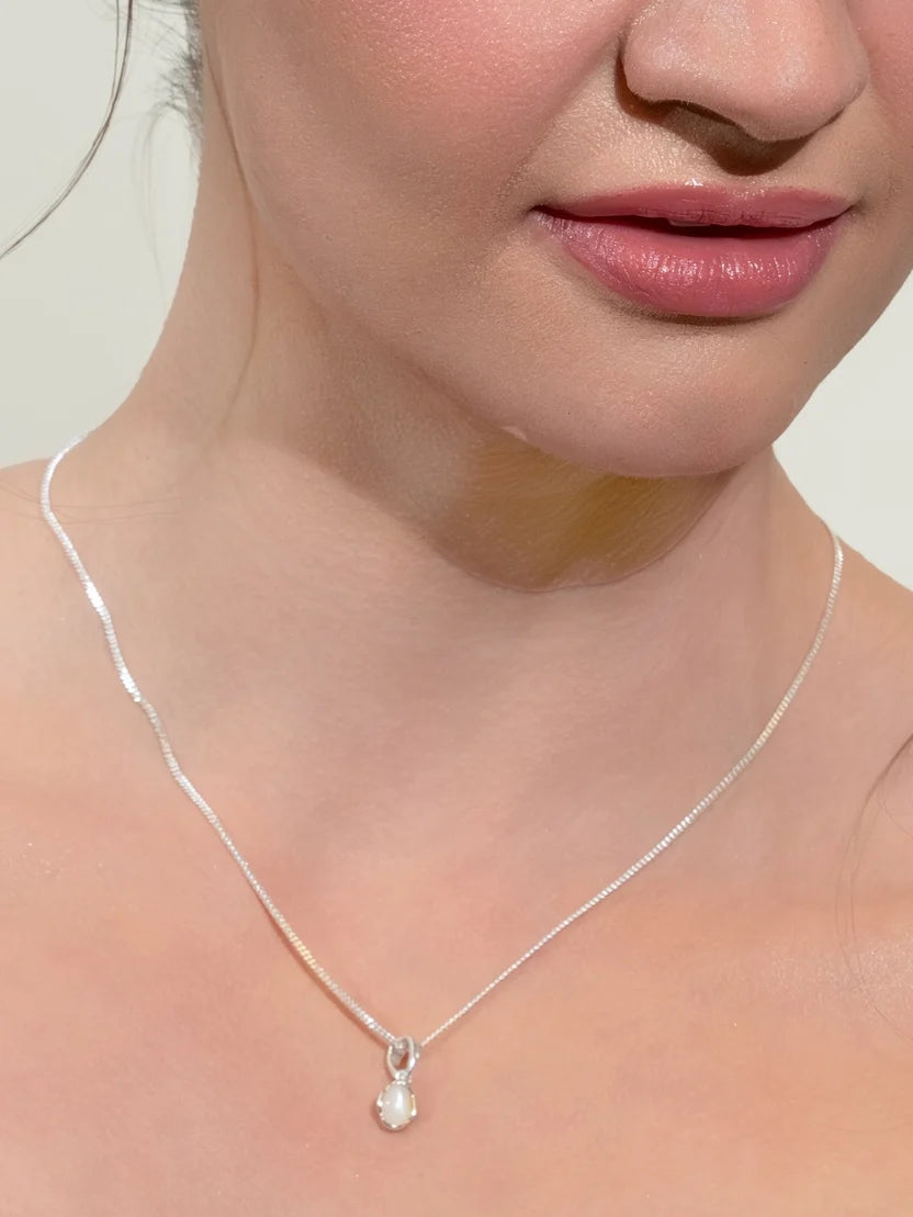 A close-up of a model's neck and lower face wearing a delicate silver chain necklace with a small white teardrop-shaped pendant.