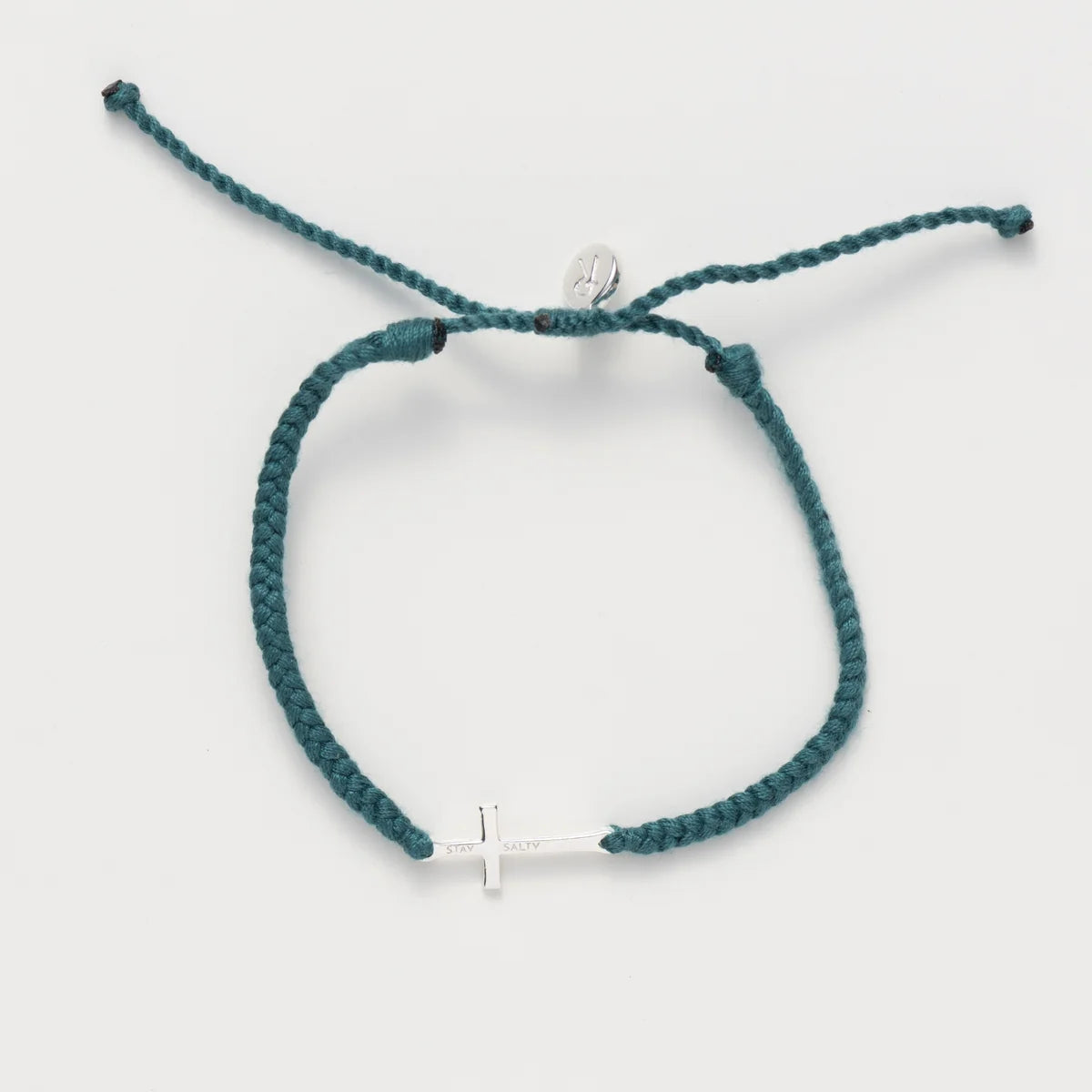A teal braided cord bracelet with a small silver cross charm and a silver circular bead, displayed on a light gray background.