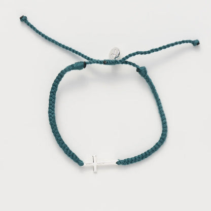 A teal braided cord bracelet with a small silver cross charm and a silver circular bead, displayed on a light gray background.