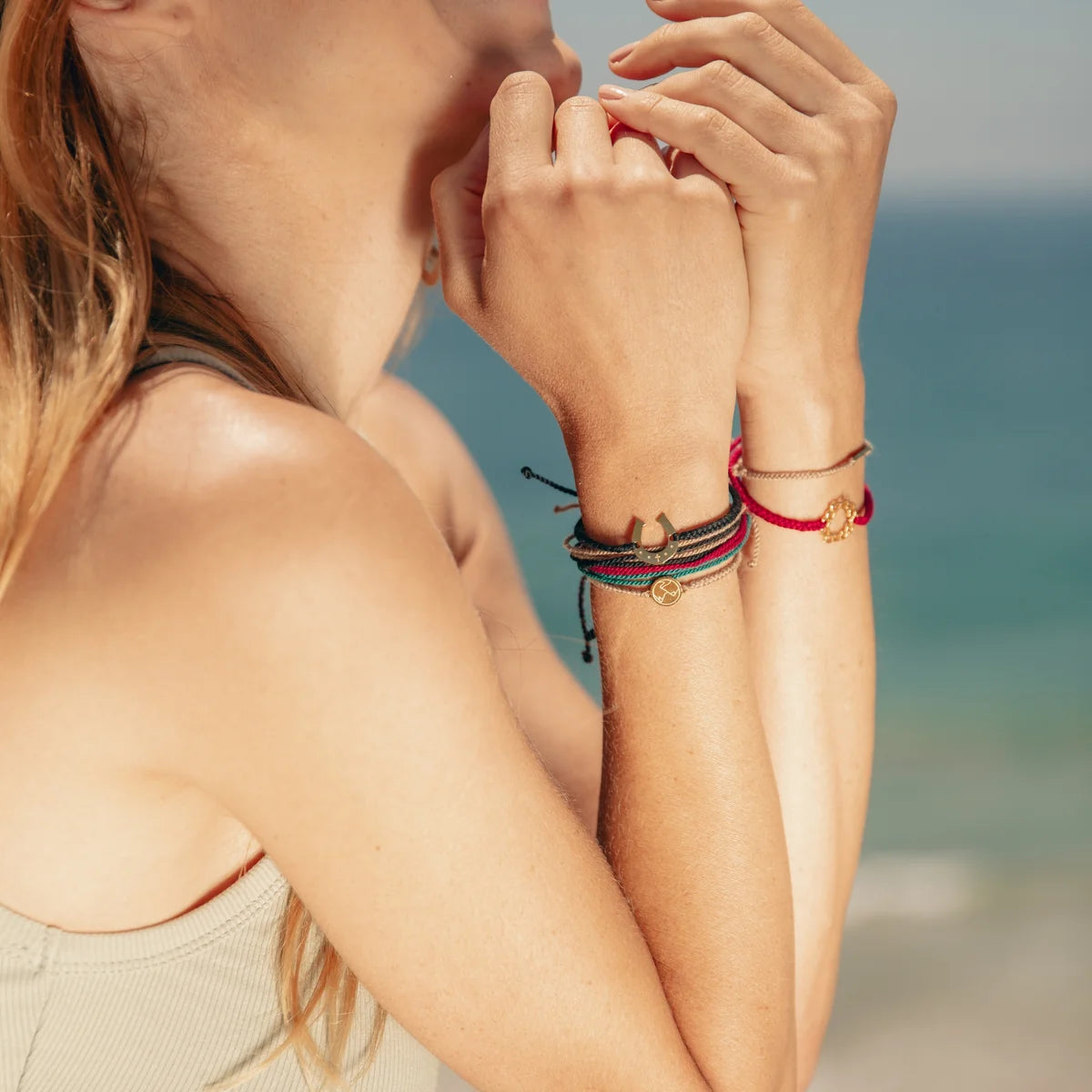 Close-up of a person's hands with bracelets on a blurred beach background