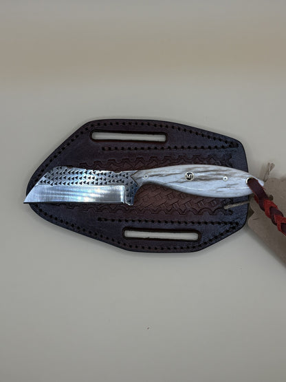 A fixed-blade knife with a hammered silver blade and a white marbled handle, resting on a dark brown textured leather sheath against a plain beige background.