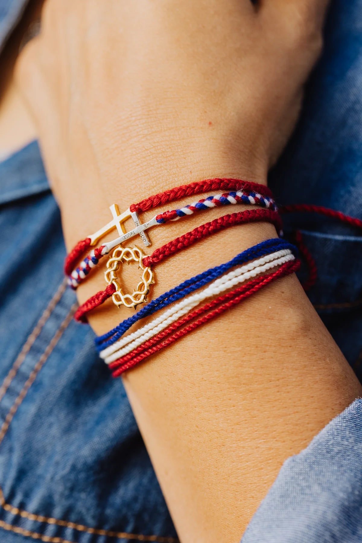 Close-up of a wrist wearing multiple bracelets with red, white, and blue strings.