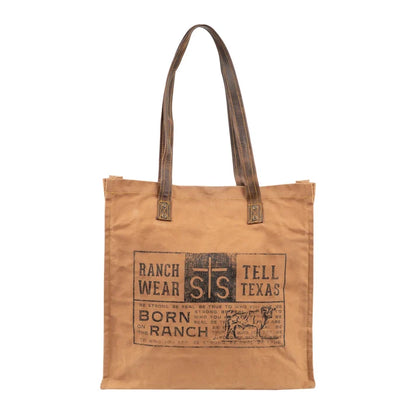 A tan canvas tote bag with dark brown leather handles and a distressed brown graphic print on the front featuring the text 'RANCH WEAR', 'STS', and 'TELL TEXAS'.