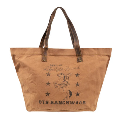 A tan canvas tote bag with dark brown leather handles and a distressed brown graphic print featuring a cowboy on a bucking horse and the text 'STS RANCHWEAR'.