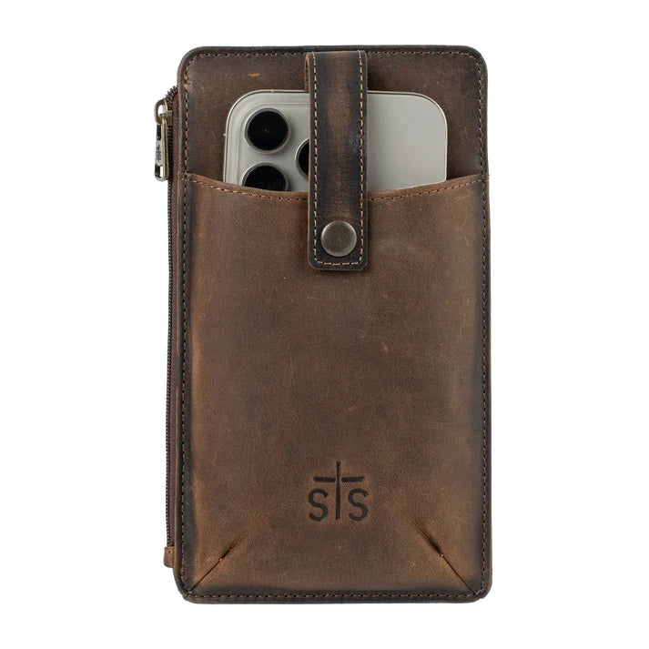 A brown distressed leather phone pouch with a front slip pocket holding a silver smartphone, featuring a snap-button strap closure and an embossed 'sts' logo on the lower front, set against a plain white background.