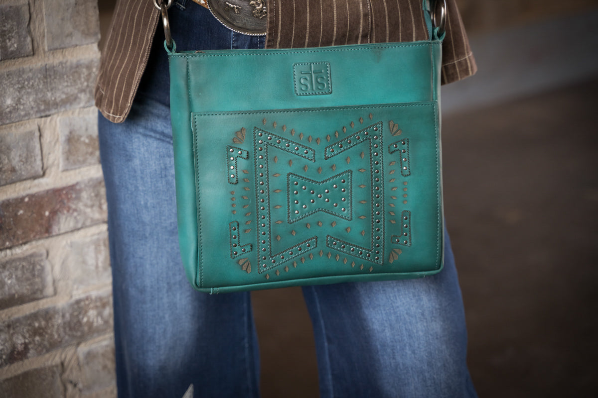 Turquoise leather crossbody purse with studded western design front view worn by woman
