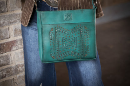 Turquoise leather crossbody purse with studded western design front view worn by woman