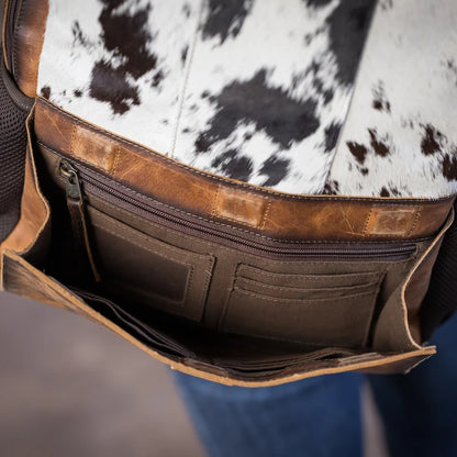 Close-up of a brown leather bag with a black and white cowhide pattern interior, showing zippered compartments and pockets.