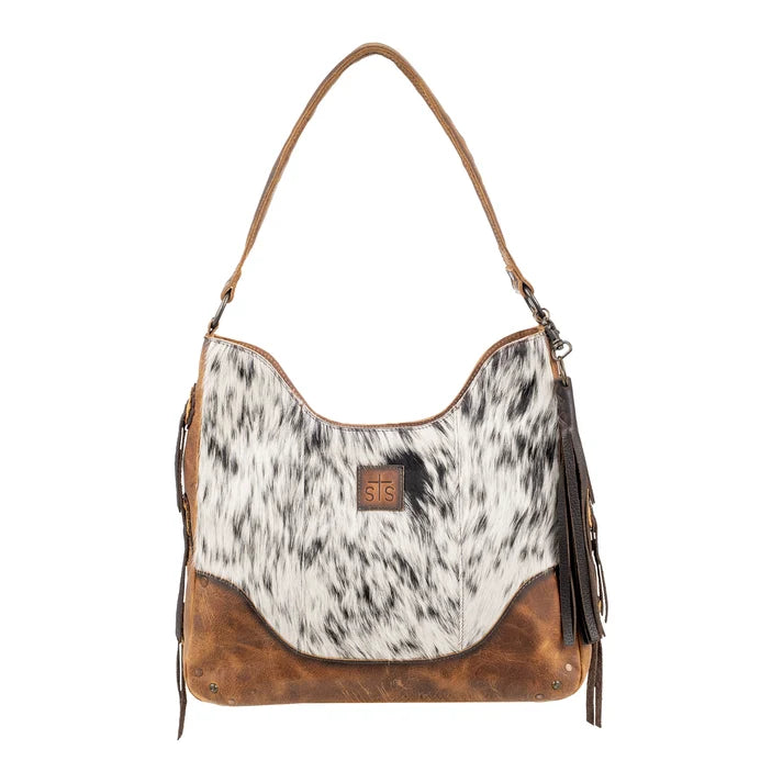 A western-style shoulder bag featuring a black and white cowhide pattern upper body, brown leather trim and base, and dark brown leather fringe tassels on the sides. A small brown leather logo patch with '315' is visible on the front.