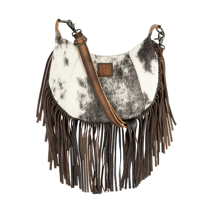 A crescent-shaped shoulder bag featuring a cowhide pattern upper section, a brown faux-leather strap, and long dark brown fringe hanging from the bottom, shown against a plain white background.