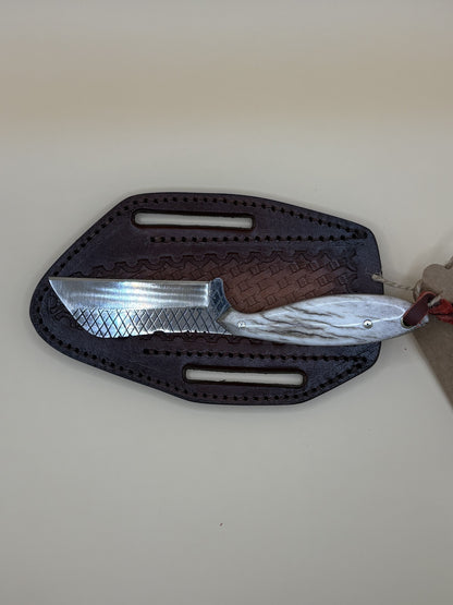 A fixed-blade knife with a textured silver blade and brown handle, partially inserted into a dark brown leather sheath on a beige background.