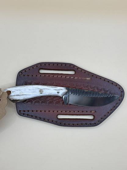 A fixed-blade knife with a textured silver handle and a dark steel blade, resting on a dark brown leather sheath with a beige background.