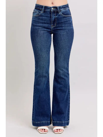 A person wearing dark blue high-rise flare jeans with white slide sandals, shown from the waist down against a light gray studio background.