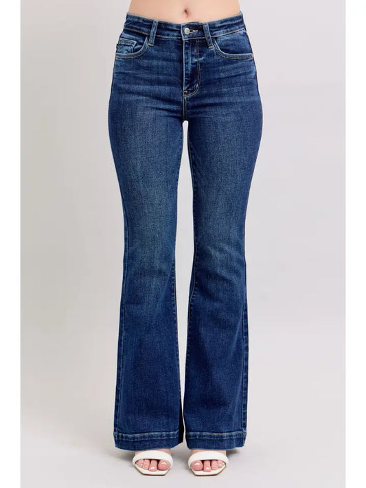 A person wearing dark blue high-rise flare jeans with white slide sandals, shown from the waist down against a light gray studio background.