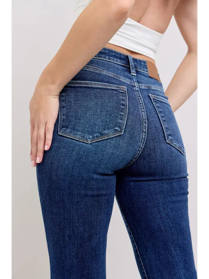 Rear view of a person wearing dark blue denim jeans with a white cropped top, showing the back pockets and waistband details.